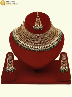 Premium matte gold bridal necklace set with ruby and green stones, heavy choker design, hanging green beads, matching earrings and maang tikka displayed on red stand, Ishwar Arts and Crafts