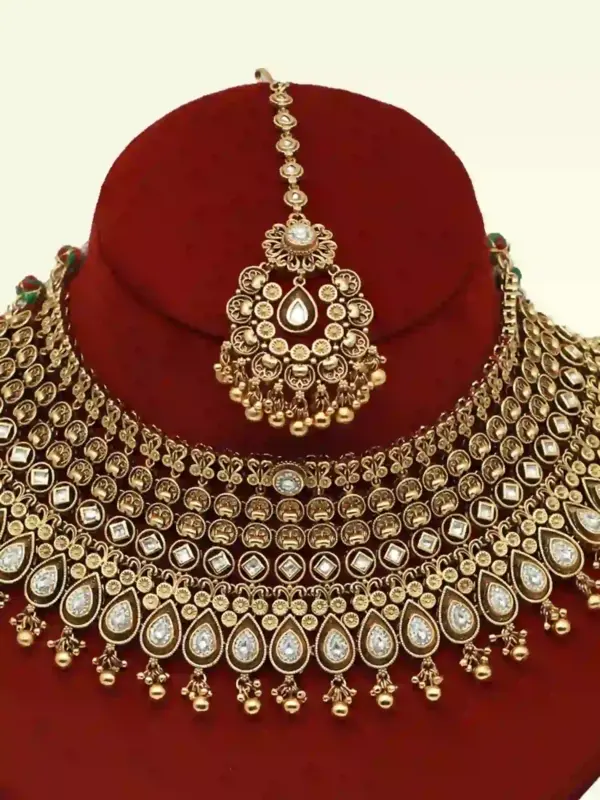 Antique gold brass bridal necklace set with Kundan stones, matching earrings, and maangtika on red display, Ishwar Arts and Crafts