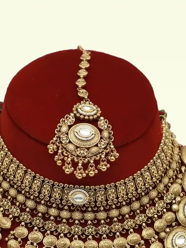 Heavy matte gold brass bridal necklace set with kundan stones, earrings, and maang tikka displayed on red jewelry stand