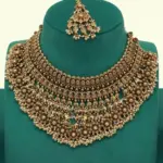 Antique gold intricate carving bridal necklace set with matching heavy earrings and maang tikka displayed on green jewelry stand