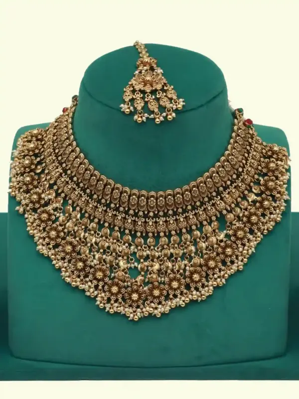 Antique gold intricate carving bridal necklace set with matching heavy earrings and maang tikka displayed on green jewelry stand