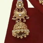 Antique gold bridal necklace set with hanging beads, matching jhumka earrings, and maangtika on red display stand