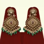Traditional matte gold necklace set with ruby stones, green beads, intricate carvings, earrings, and maang tikka displayed on red stand, Ishwar Arts and Crafts