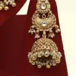 Antique gold bridal necklace set with hanging beads, matching jhumka earrings, and maangtika on red display stand