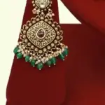 Traditional matte gold necklace set with ruby stones, green beads, intricate carvings, earrings, and maang tikka displayed on red stand, Ishwar Arts and Crafts