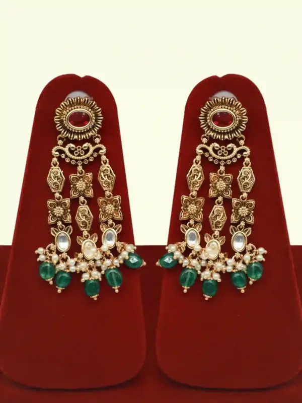 Premium matte gold bridal necklace set with ruby and green stones, heavy choker design, hanging green beads, matching earrings and maang tikka displayed on red stand