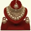 Heavy matte gold brass bridal necklace set with kundan stones, earrings, and maang tikka displayed on red jewelry stand