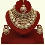Heavy matte gold brass bridal necklace set with kundan stones, earrings, and maang tikka displayed on red jewelry stand