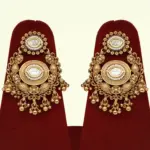 Heavy matte gold brass bridal necklace set with kundan stones, earrings, and maang tikka displayed on red jewelry stand