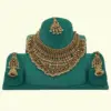 Antique gold intricate carving bridal necklace set with matching heavy earrings and maang tikka displayed on green jewelry stand