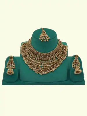 Antique gold intricate carving bridal necklace set with matching heavy earrings and maang tikka displayed on green jewelry stand