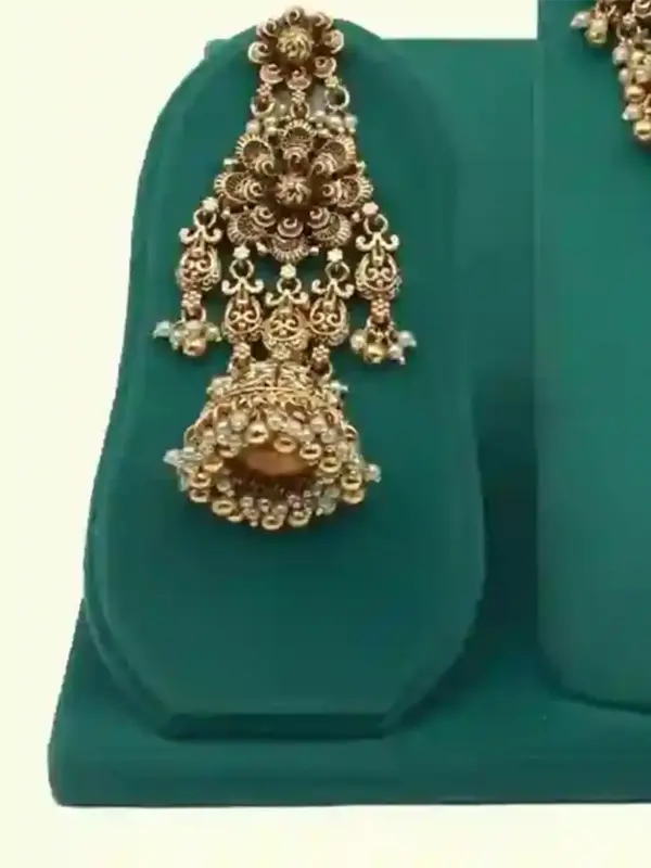 Antique gold intricate carving bridal necklace set with matching heavy earrings and maang tikka displayed on green jewelry stand