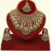 Traditional matte gold necklace set with ruby stones, green beads, intricate carvings, earrings, and maang tikka displayed on red stand