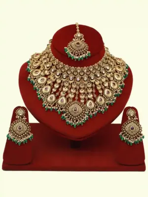 Traditional matte gold necklace set with ruby stones, green beads, intricate carvings, earrings, and maang tikka displayed on red stand