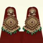 Traditional matte gold necklace set with ruby stones, green beads, intricate carvings, earrings, and maang tikka displayed on red stand