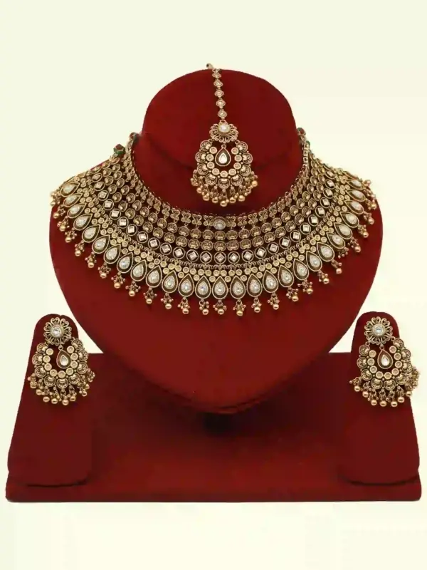 Antique gold brass bridal necklace set with Kundan stones, matching earrings, and maangtika on red display, Ishwar Arts and Crafts