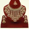 Antique gold bridal necklace set with hanging beads, matching jhumka earrings, and maangtika on red display stand