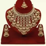 Antique gold bridal necklace set with hanging beads, matching jhumka earrings, and maangtika on red display stand