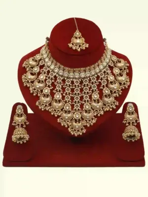 Antique gold bridal necklace set with hanging beads, matching jhumka earrings, and maangtika on red display stand
