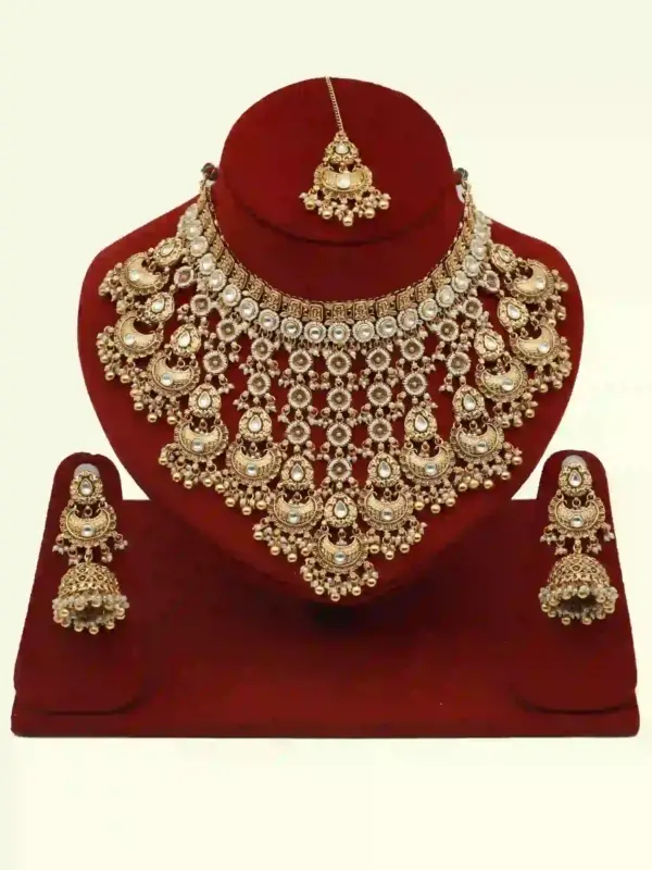 Antique gold bridal necklace set with hanging beads, matching jhumka earrings, and maangtika on red display stand