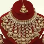 Antique gold bridal necklace set with hanging beads, matching jhumka earrings, and maangtika on red display stand