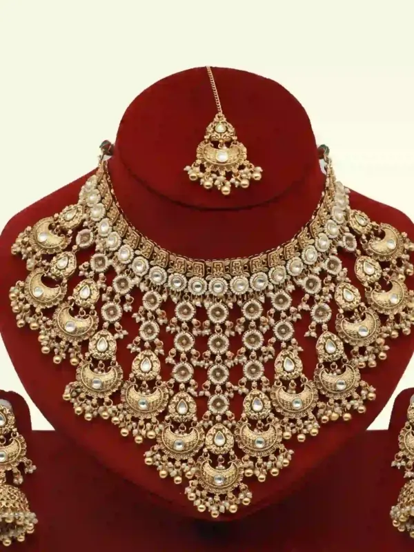 Antique gold bridal necklace set with hanging beads, matching jhumka earrings, and maangtika on red display stand